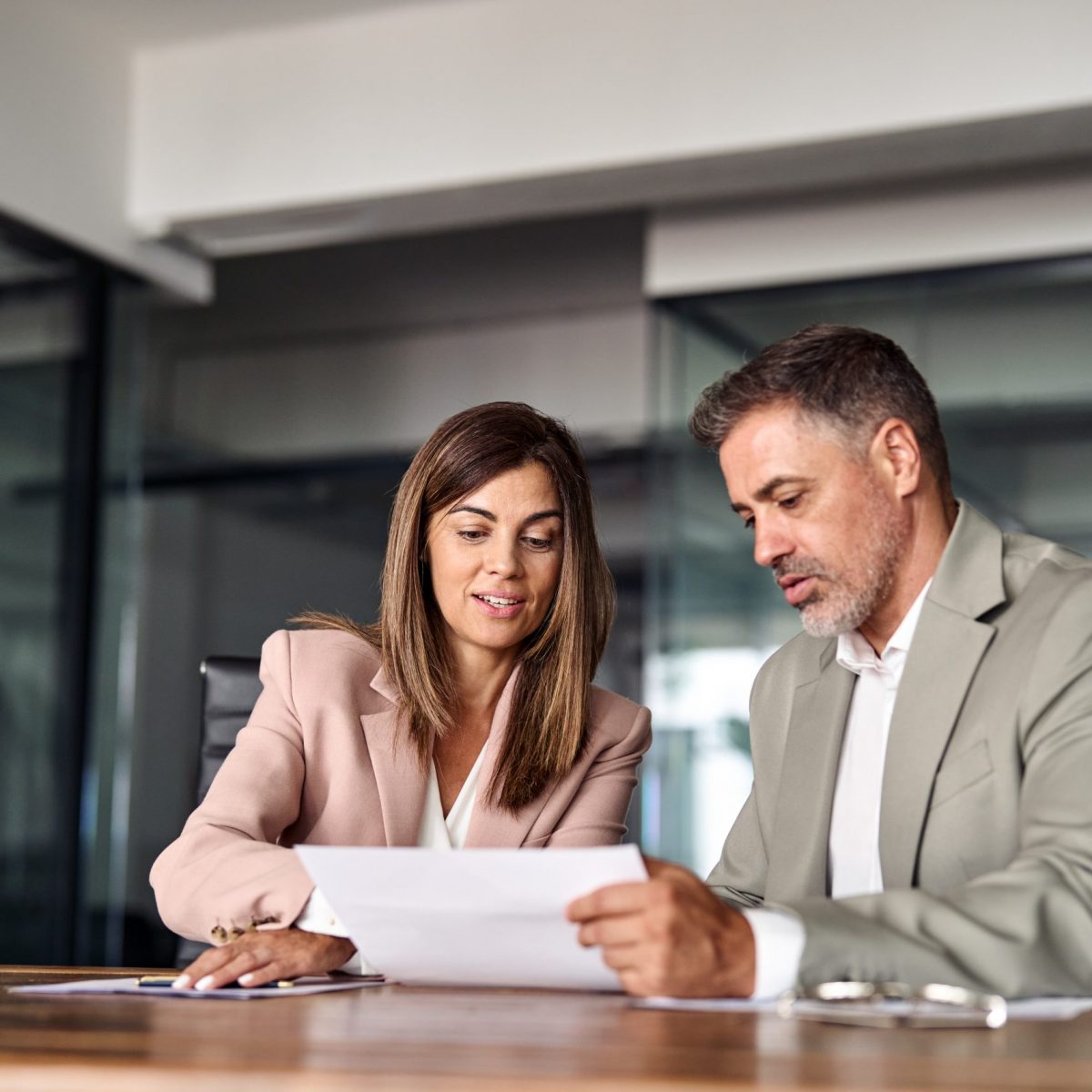 Two professional executives discussing financial accounting papers working together in office. Mature business woman manager consulting older man client holding legal documents at meeting.